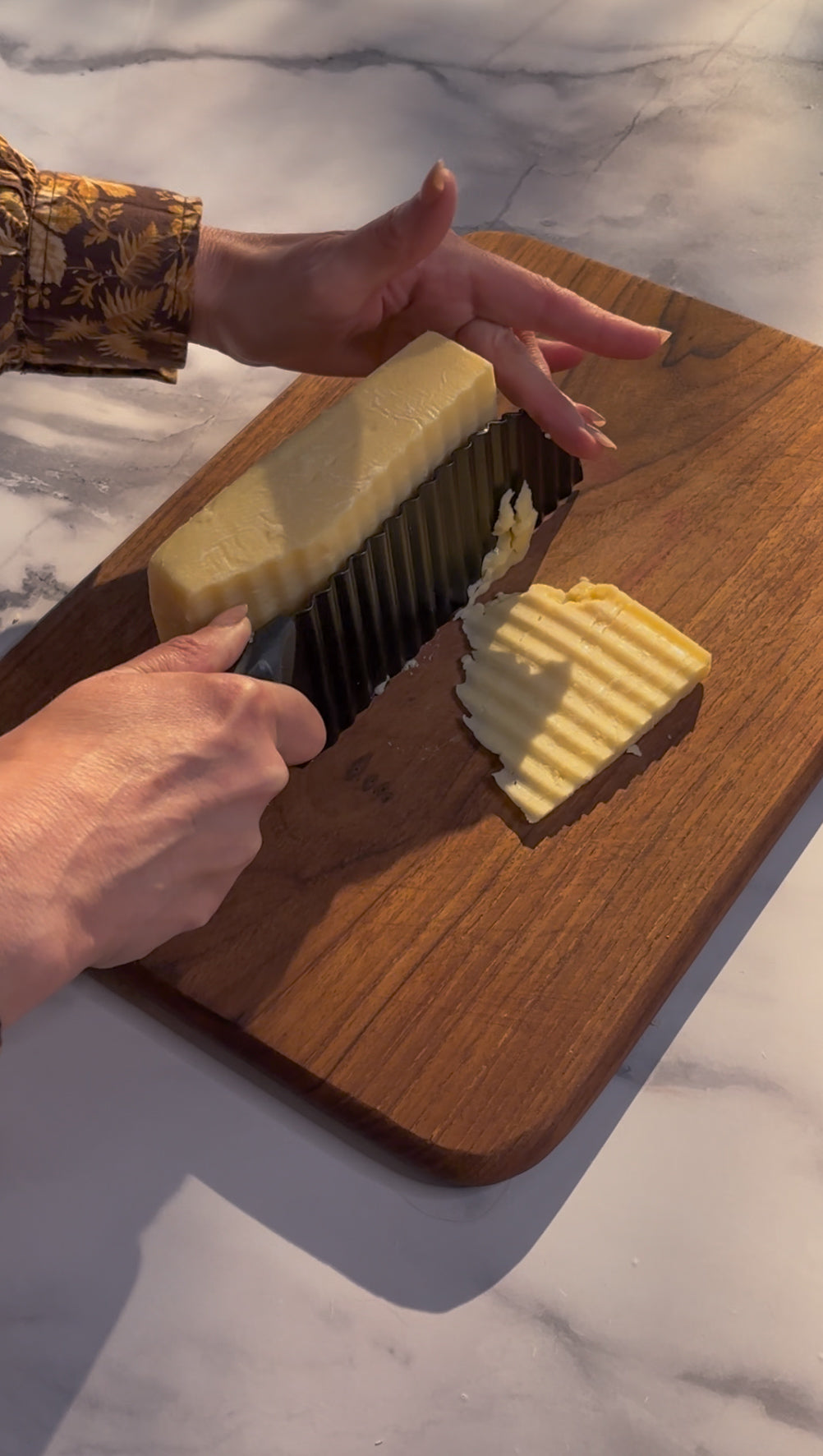 Cheddar cheese being slices on a board