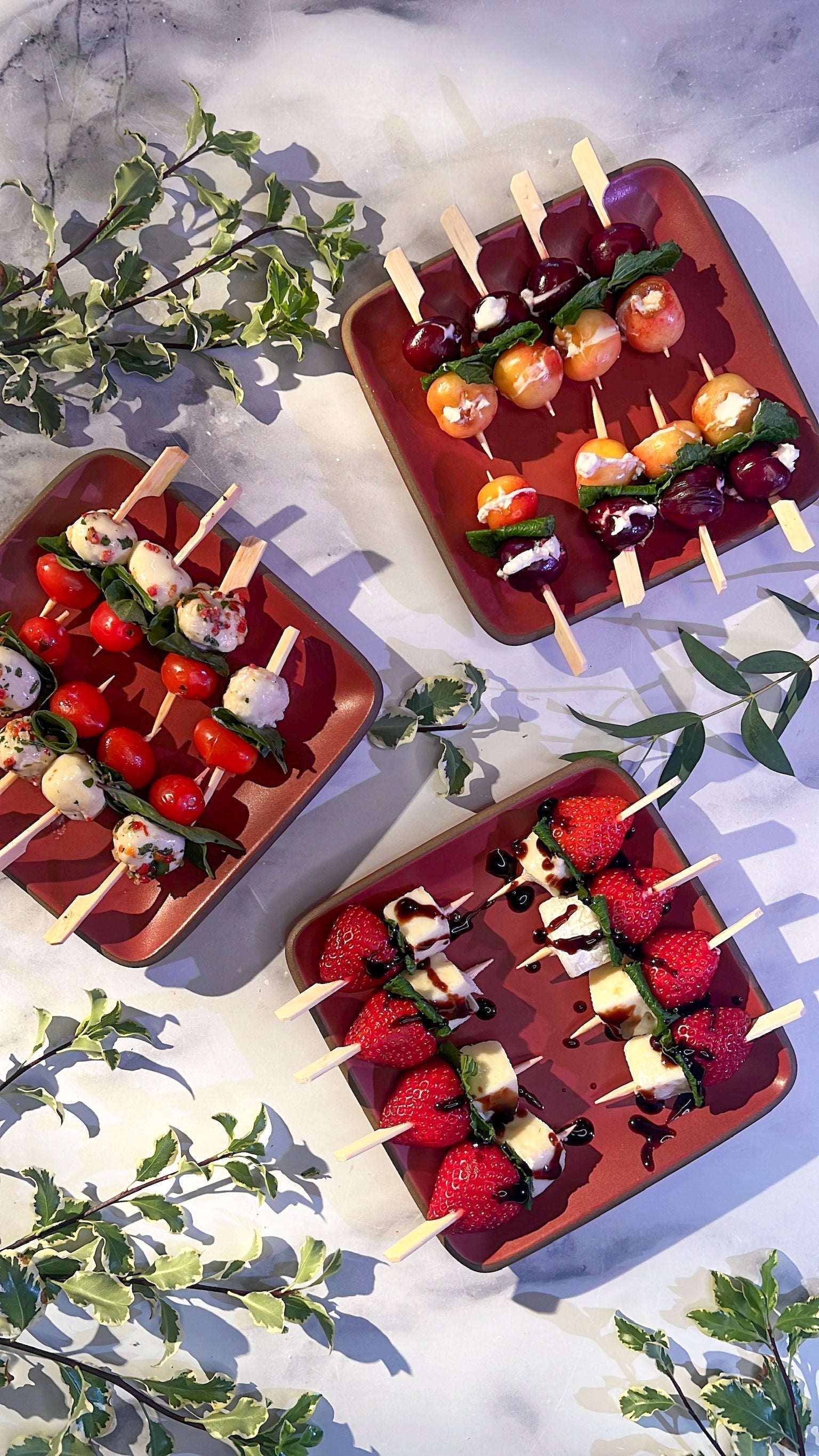 skewers for a summer party displayed on trays surround by different types of greenery