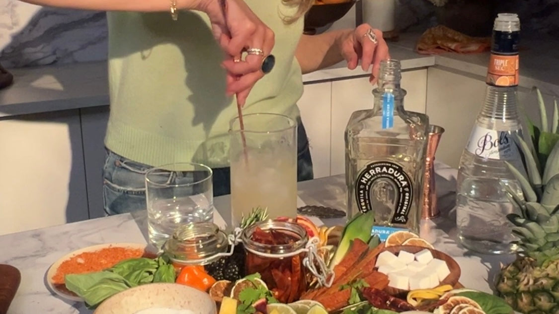 stirring margarita with ladle with platter of ingredients and tequila