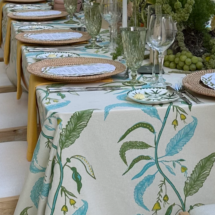 cream green and blue tablecloth with floral design styled with candles, place settings, and fruit