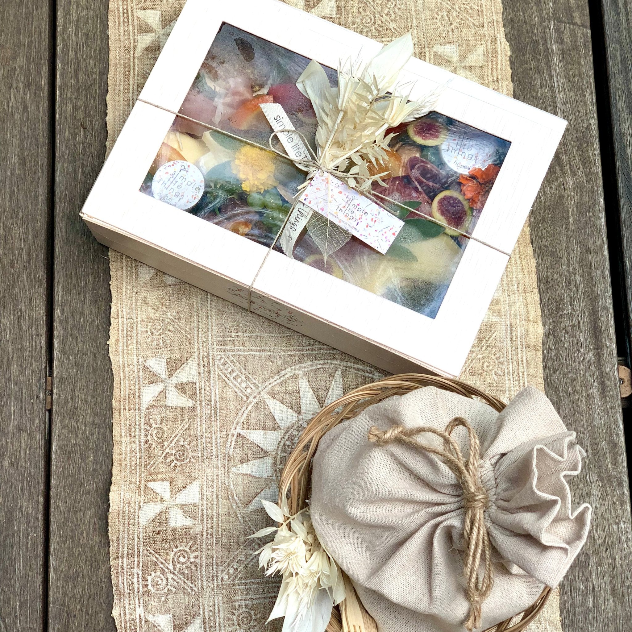 cheese and charcuterie gift box with crackers wrapped in a napkin and placed in a basket. photographed on a cream runner with star shaped design on a wooden counter