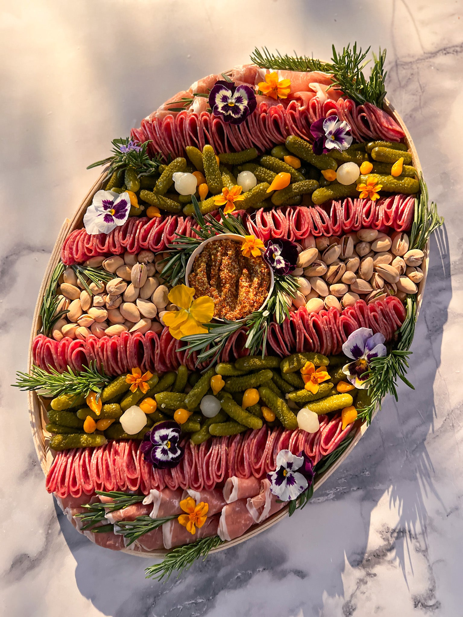 Decorative platter shaped like an avocado with various foods arranged inside on a marble surface.