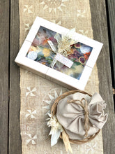 Load image into Gallery viewer, cheese and charcuterie gift box with crackers wrapped in a napkin and placed in a basket. photographed on a cream runner with star shaped design on a wooden counter

