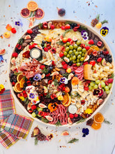 Load image into Gallery viewer, cheese and  charcuterie board overhead on counter top surrounded by dried fruit and herbs and a napkin
